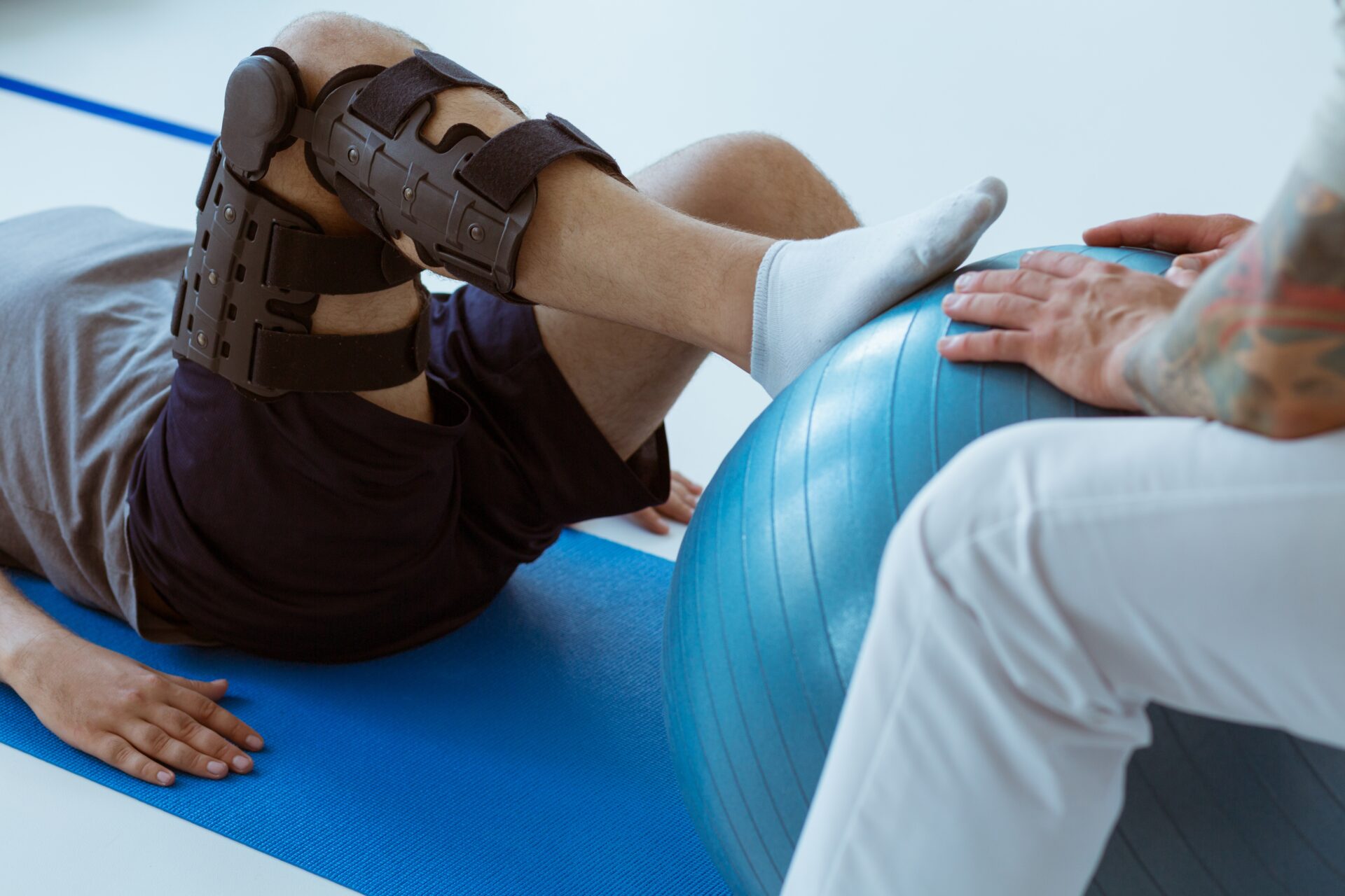 Physiotherapy - Pretty patient sitting on the blue mat in the gym and training with the ball